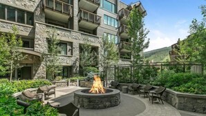 A multi-story building with balconies, a stone facade, and a circular outdoor seating area with a fire pit. - Vail Lion 1 Bedroom Mountain Vacation Rental Just Steps From the Eagle Bahn Gondola (Vail)