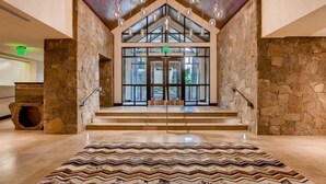 A spacious lobby with a stone wall, a patterned rug, and a staircase leading to an entrance. - Vail Lion 1 Bedroom Mountain Vacation Rental Just Steps From the Eagle Bahn Gondola (Vail)