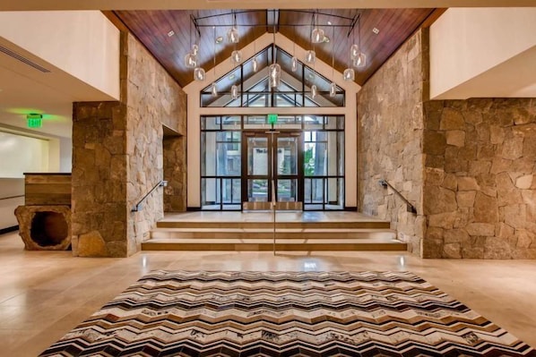A spacious lobby with a stone wall, a patterned rug, and a staircase leading to an entrance.