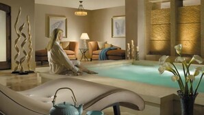 Uma área de spa tranquila com uma cadeira de massagem, uma pequena mesa com um bule e xícara, uma poltrona, um sofá e um vaso decorativo com flores.