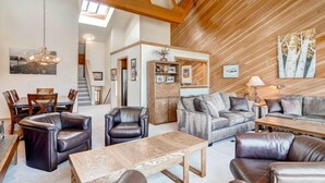 A spacious living room with a high ceiling, wooden beams, a dining area with a table and chairs, and a cozy seating area with sofas and a coffee table. - Lakeside Village 4 Bedroom Condo (Keystone)