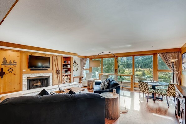 A spacious living room with a fireplace, a television, and a large window offering a view of the outdoors. - Lakeside Village 4 Bedroom Condo (Keystone)