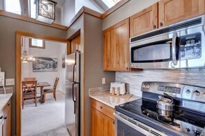 A modern kitchen with wooden cabinets, stainless steel appliances, and a dining area with a chandelier. - Lakeside Village 4 Bedroom Condo (Keystone)