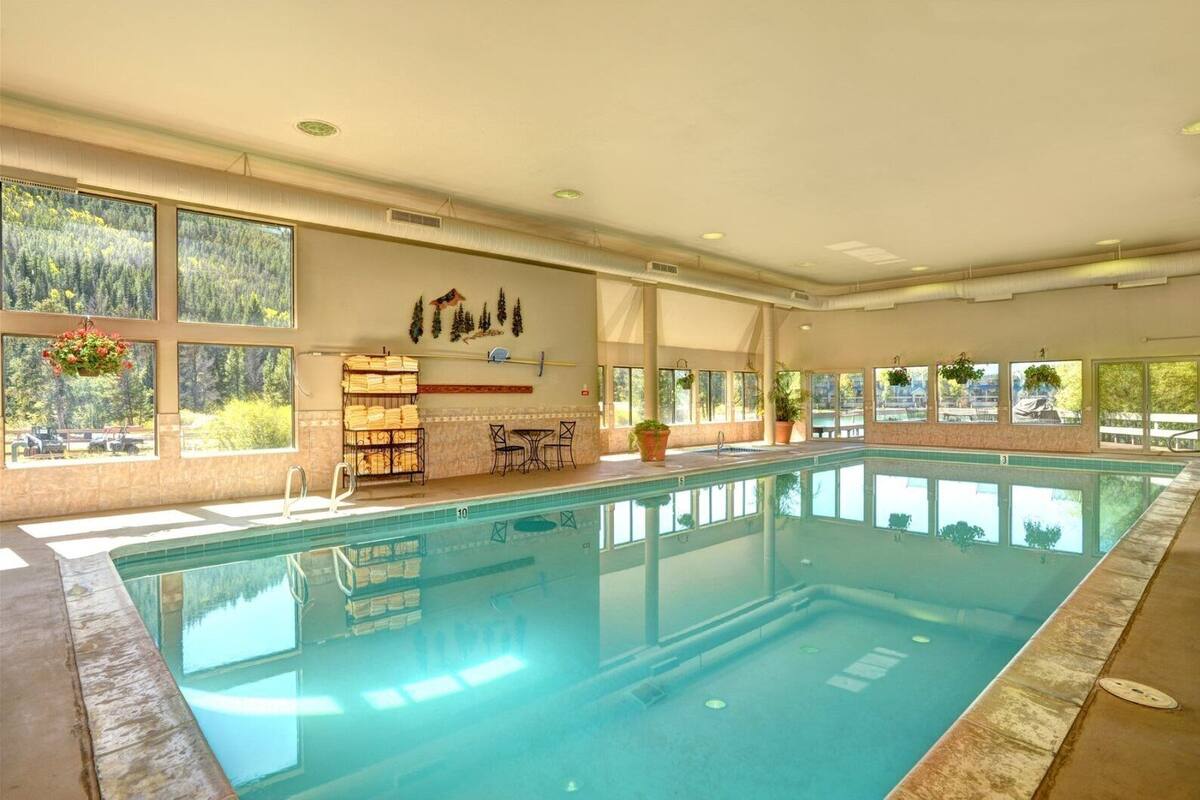An indoor swimming pool with clear views of the surrounding forest through large windows.