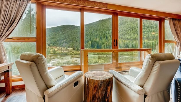 A room with large windows offering a view of a forested hillside. There are two leather chairs and a small wooden table. - Lakeside Village 4 Bedroom Condo (Keystone)