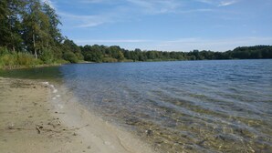 Een helder meer met een zandstrand en een dicht bos op de achtergrond.