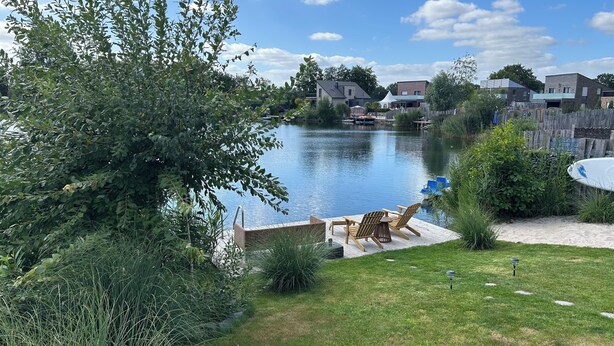 Een achtertuin met een houten terras, een klein zwembad en een uitzicht op een meer en huizen op de achtergrond.