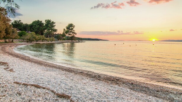 A beach with pebbles, trees, and a sunset over the water. - Authentic Villa With Pool on the Island of Brac, Near the Beach (Supetar)