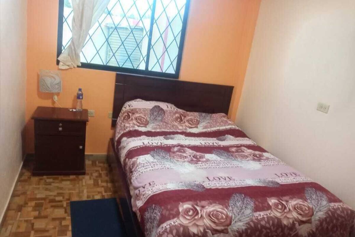 A bedroom with a bed, a nightstand, a window with curtains, and a wooden floor.