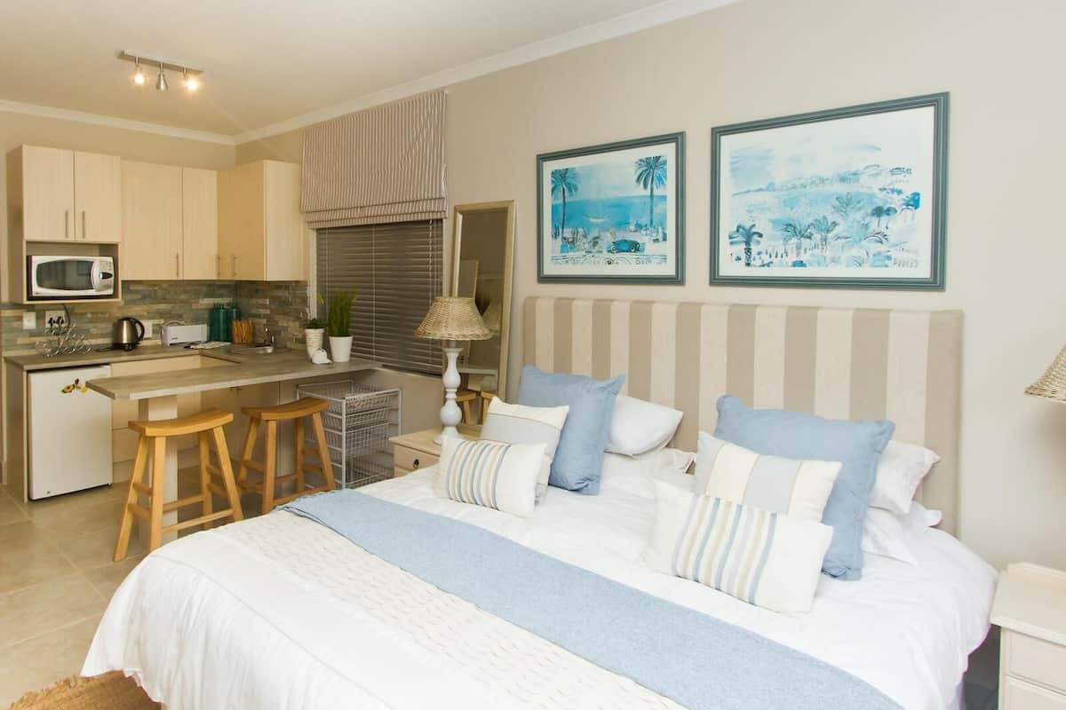 A bedroom with a large bed, a small kitchenette, and two framed artworks on the wall.