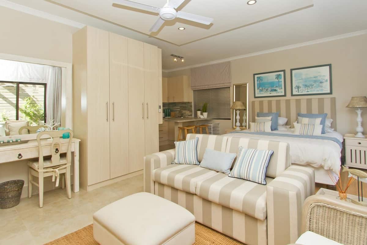 A bedroom with a bed, a striped sofa, a desk, and a ceiling fan.