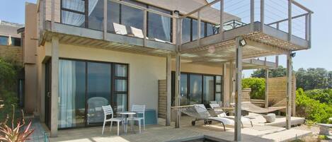 A modern two-story house with a patio, outdoor seating, and a garden area.