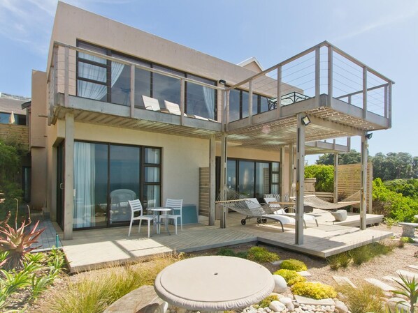 A modern two-story house with a patio, outdoor seating, and a garden area.