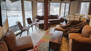 A cozy living room with a fireplace, large windows, and a view of a river. - Relax Swim and BBQ at Sierra River House (Three rivers)