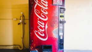 A Coca-Cola vending machine against a yellow wall. - Express Inn Gulf Bank (Houston)
