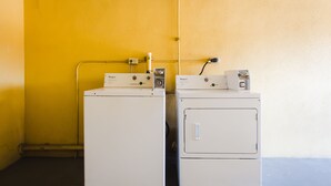Two white Whirlpool washers in a laundry room with a yellow wall and a blue floor. - Express Inn Gulf Bank (Houston)