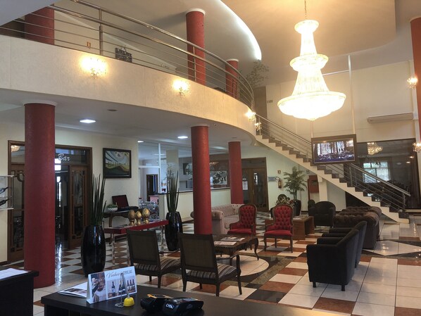 A spacious lobby with a high ceiling, a grand chandelier, a staircase, and a bar area.