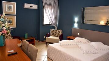 Habitación de hotel con cama, escritorio, silla, mesita y ventana con cortinas.