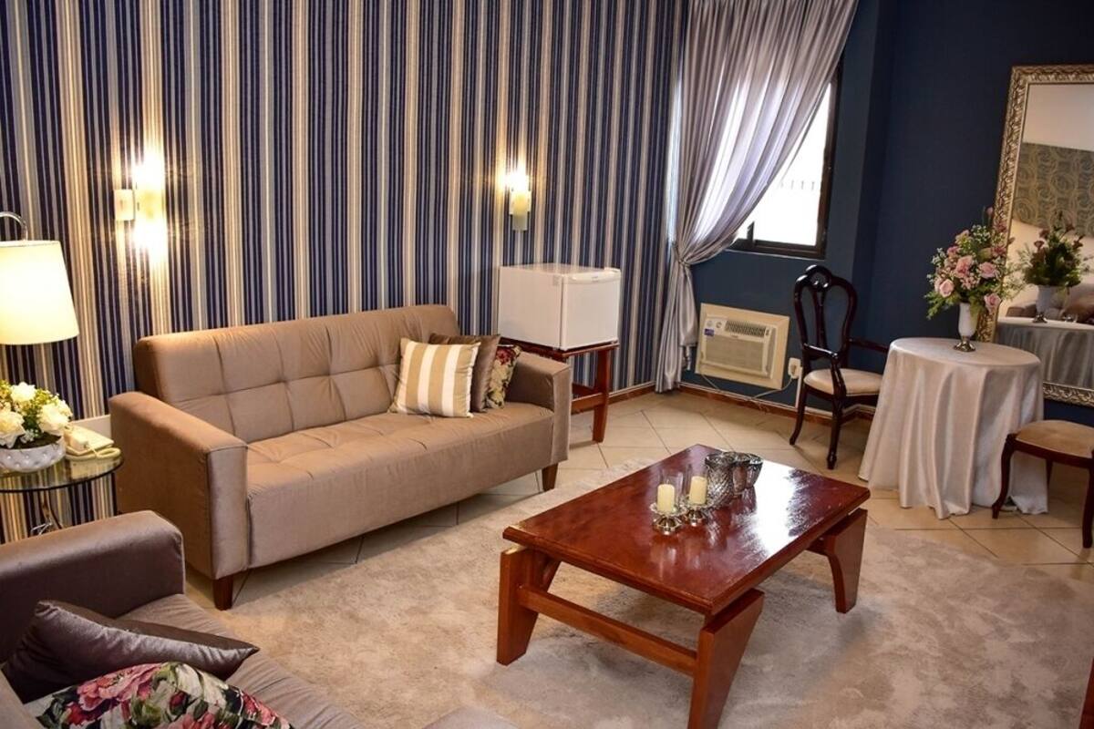 A living room with a beige sofa, a wooden coffee table, a side table with a lamp, and a striped wall.