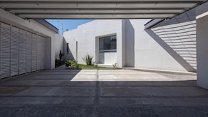 A modern, minimalist outdoor space with a concrete floor, a covered area with a metal roof, and a small garden with plants. - Gorgeous 3 bed/3bath home in the heart of Ensenada! (Ensenada)