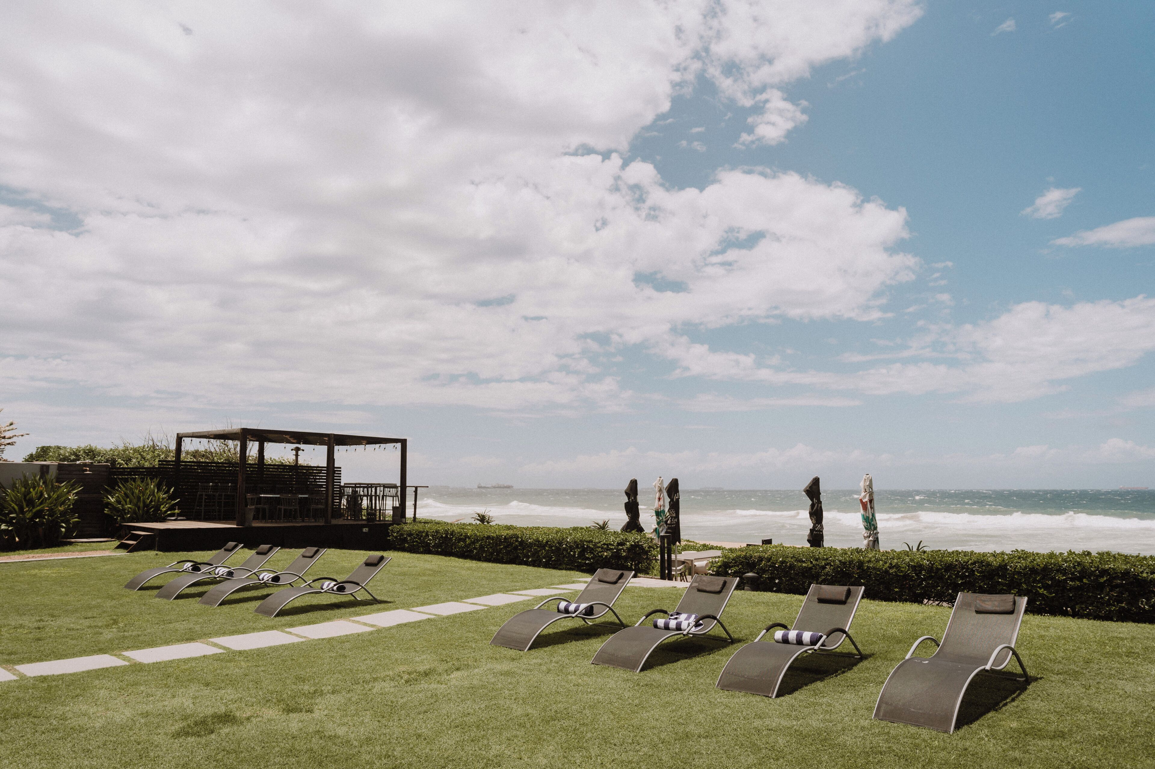 Ein Strandloungebereich mit Liegestühlen und einer überdachten Sitzecke mit Blick auf den Ozean.