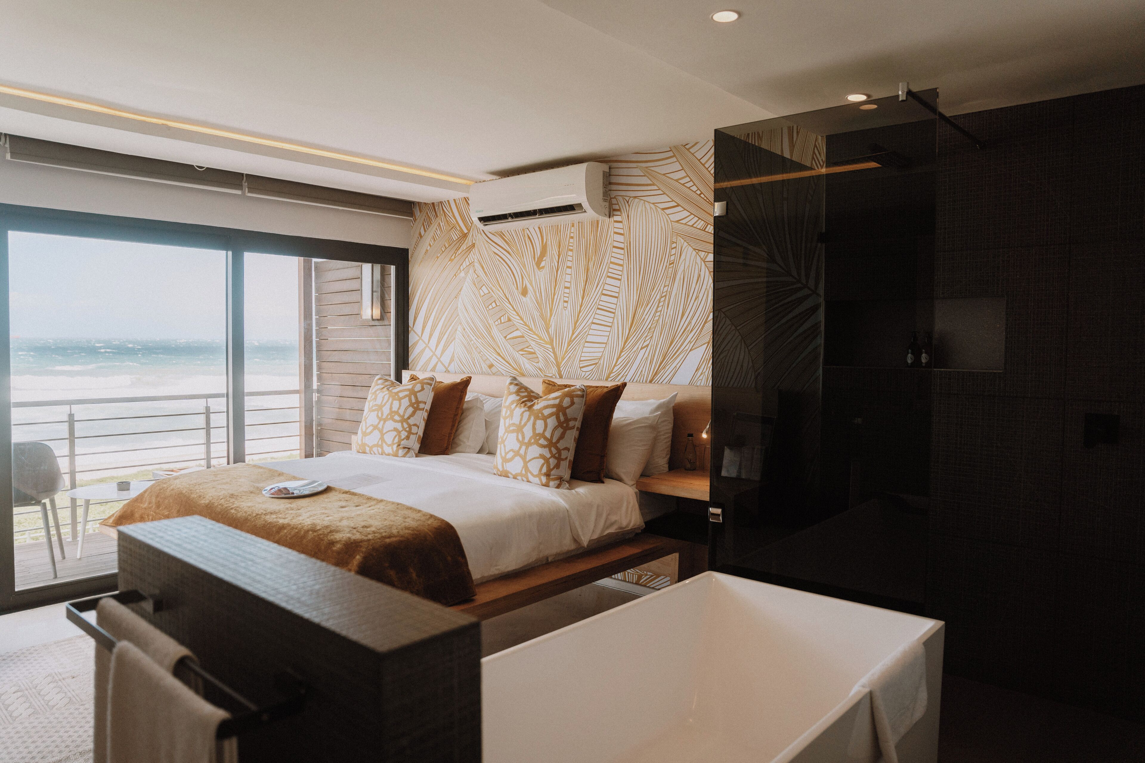 A modern bedroom with a large bed, a bathtub, and a view of the ocean.