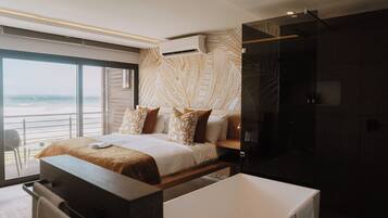 A modern bedroom with a large bed, a bathtub, and a view of the ocean.