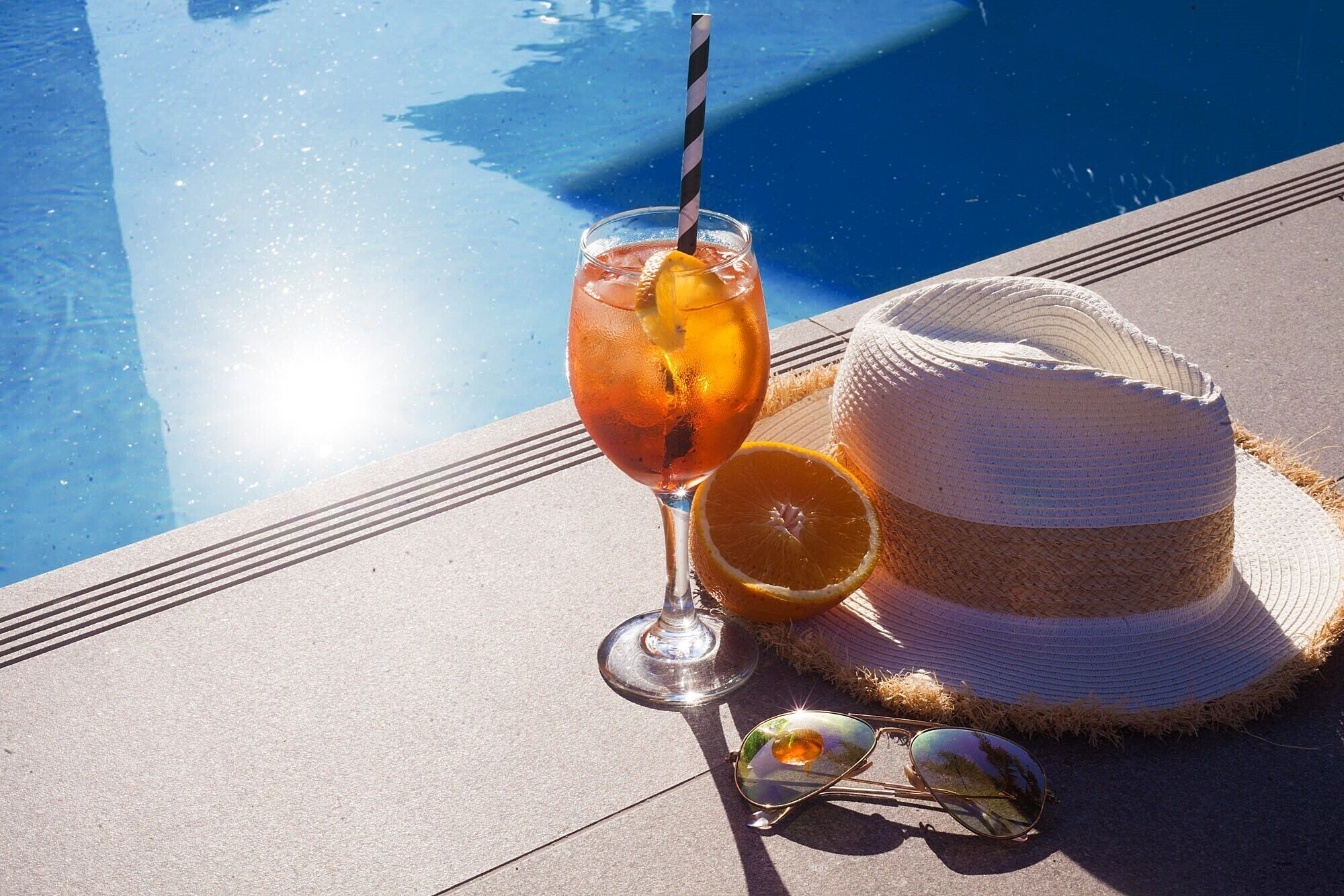 Un vaso de té helado con pajita, un sombrero de paja y una rodaja de naranja en la terraza de la piscina.