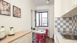 A compact kitchen with a window, a tiled backsplash, and a dining area with red chairs. - Casa Cosi - Maria Novella (Firenze)