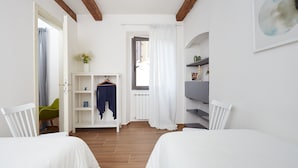 A bedroom with two beds, a wardrobe, a chair, and a shelf with decorative items. - Casa Cosi - Maria Novella (Firenze)