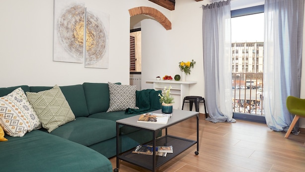 A living room with a green sofa, a coffee table, and a view of the city through large windows. - Casa Cosi - Maria Novella (Firenze)