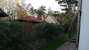 Un camí de maó estret que condueix a una casa amb teulada vermella, envoltada de vegetació densa i una paret de pedra.