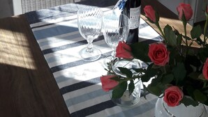 Una mesa de comedor con una botella de vino, dos copas y un florero con rosas.