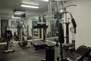Un gimnasio con equipos de ejercicio variados, incluyendo una caminadora, máquinas de pesas y pesas libres.