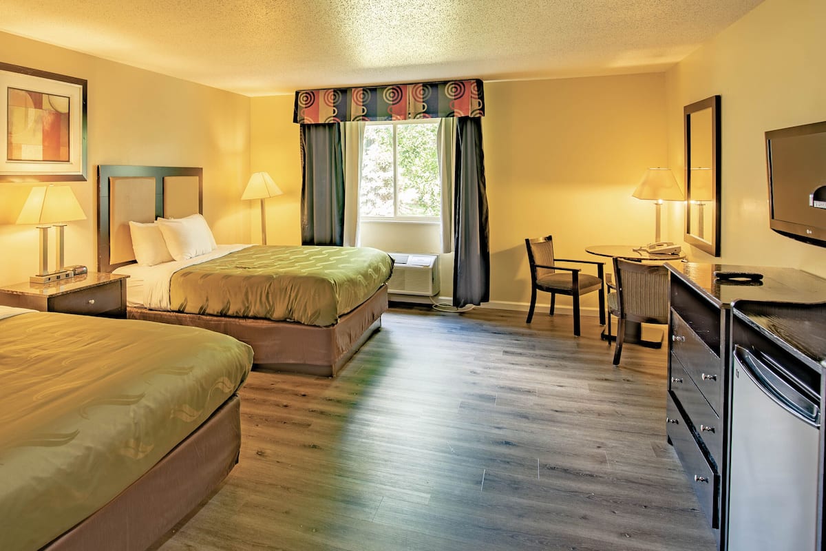 A hotel room with two beds, a desk, a chair, a television, and a window with curtains.
