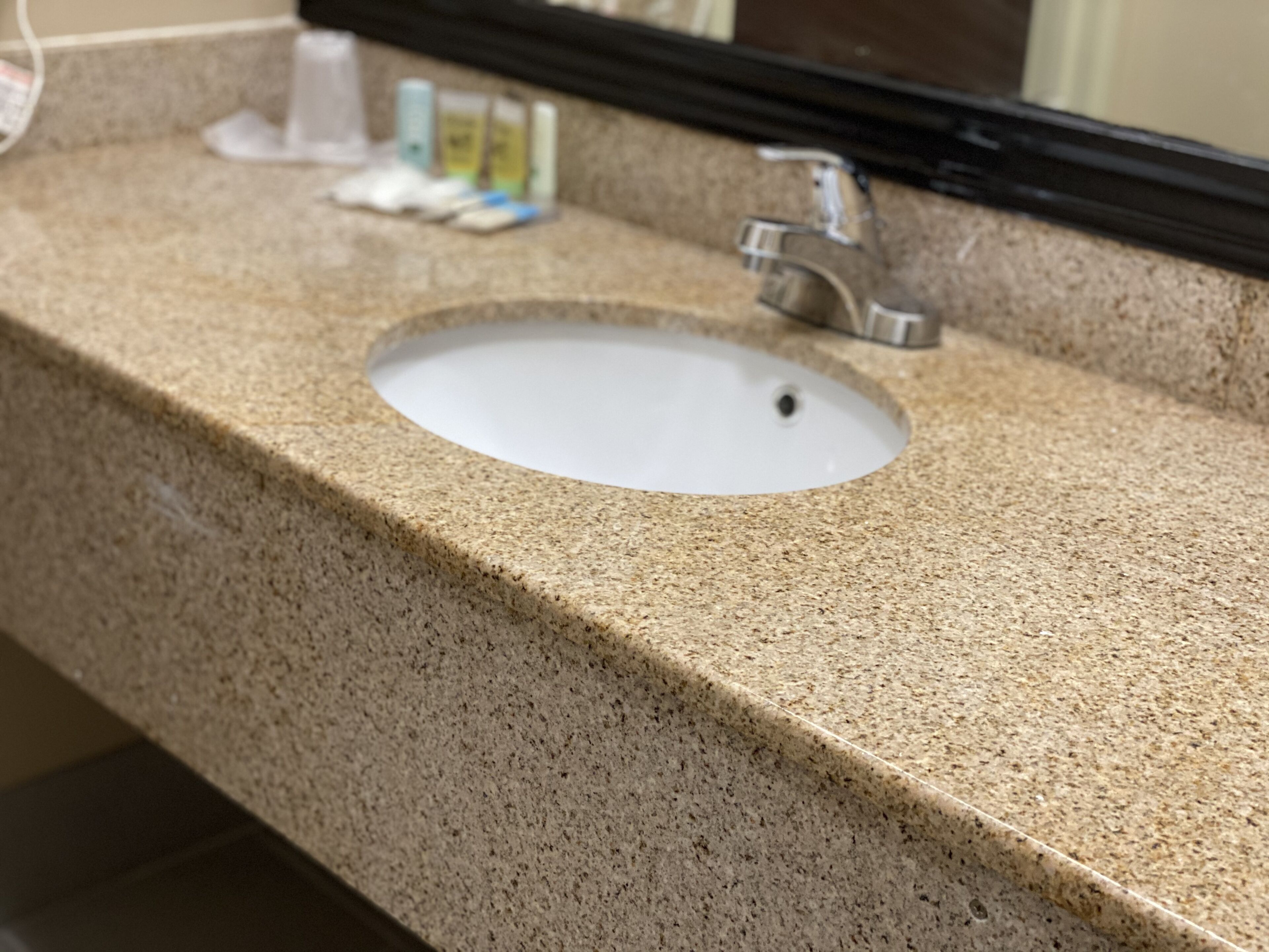 A bathroom sink with a granite countertop and a mirror above it.