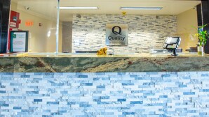 Un comptoir d’accueil d’hôtel avec un mur décoré de mosaïques, une enseigne indiquant « Qualité garantie par Choice Hotels » et une plante posée sur le comptoir.