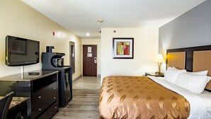 Une chambre d’hôtel avec un lit, un bureau avec une télévision, une machine à café et un tableau au mur.