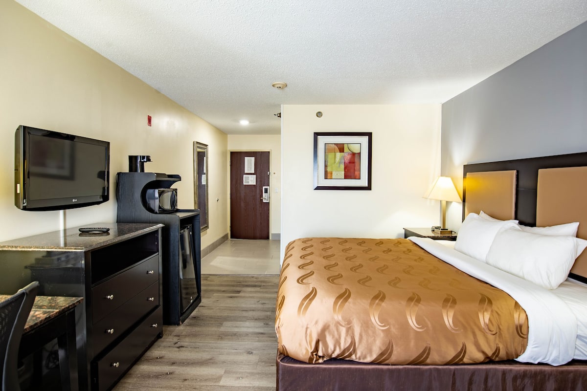 A hotel room with a bed, a desk with a television, a coffee maker, and a painting on the wall.