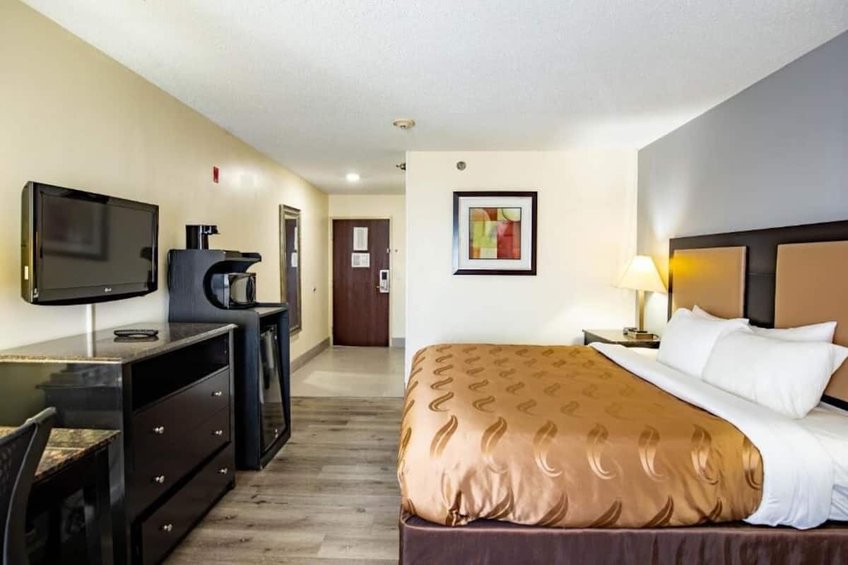 A hotel room with a bed, a desk with a television, a coffee maker, and a framed picture on the wall.