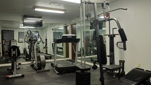 Une salle de sport équipée de divers appareils d’exercice, d’un tapis de course et d’un mur entièrement recouvert de miroirs.