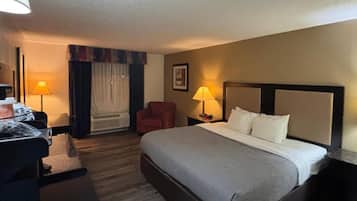 Habitación de hotel con cama, dos lámparas de noche, una silla, escritorio con lámpara y ventana con cortinas.