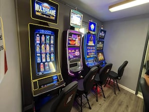 A row of slot machines with various game titles, including 'MULTI-GAME' and 'VELOCITY,' in a room with chairs. - Quality Inn & Suites Woodstock near Lake Geneva (Woodstock)