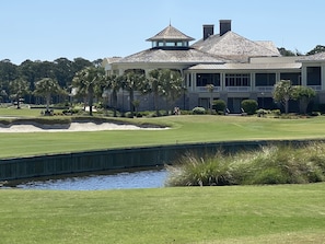 A golf course with a water hazard, a clubhouse, and a large building with a tower.