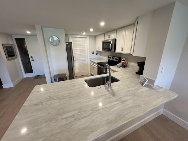 A modern kitchen with a central island, stainless steel appliances, and a clock on the wall.