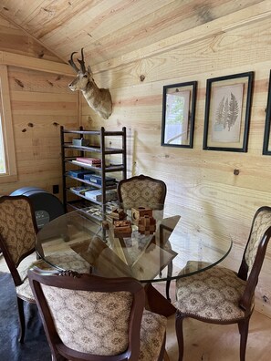 A wooden interior with a glass table surrounded by patterned chairs, a ladder, and framed botanical prints on the wall.