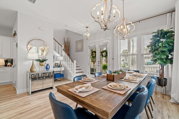A dining area with a wooden table set for four, blue chairs, and a chandelier. - We have electricity and ready for a renter. Beach 3 min walk, west end PCB (Panama City Beach)