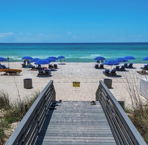 A beach with a wooden walkway leading to the shore, equipped with blue umbrellas and sun loungers. - We have electricity and ready for a renter. Beach 3 min walk, west end PCB (Panama City Beach)