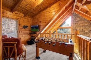 A cozy wooden cabin with a foosball table, a comfortable seating area, and a stone wall. - February Specials! Hot Tub, Cozy Fireplace, 1mile to Pkwy, 2P Arcade Games (Pigeon Forge)