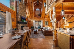 A rustic cabin interior with a dining area, living room, and kitchen. - February Specials! Hot Tub, Cozy Fireplace, 1mile to Pkwy, 2P Arcade Games (Pigeon Forge)